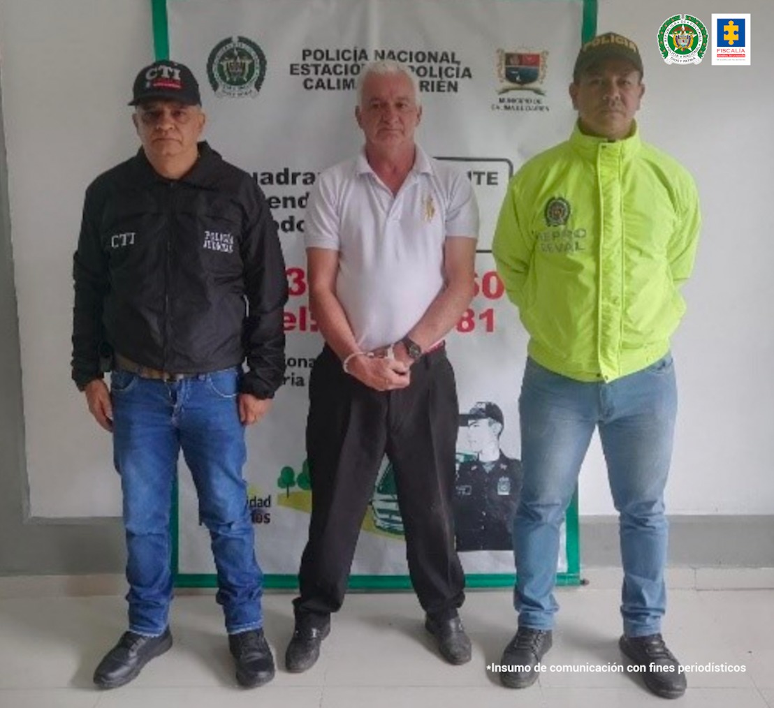 Aparece el hoy imputado, vestido con camisa oscura y jean; con brazos atrás y agachado; acompañado de dos integrantes de la Policía Nacional a lado y lado. Delante de él, hay una mesa con elementos incautados como dos celulares, una pistola, munición y dos proveedores. Asimismo, se ve parte de una motocicleta, igualmente incautada.