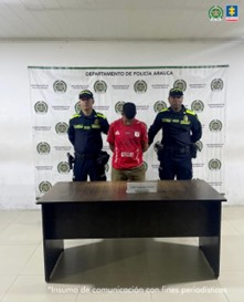 Se visualiza al capturado junto a dos uniformados de la Policía Nacional. Detrás de ellos el banner que identifica a la Policía Nacional