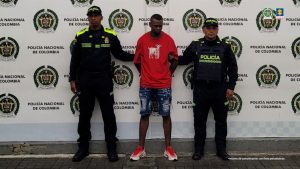 En la fotografía aparece de pie y con los brazos atrás, Ronald Stiven Paz Ramos. Viste con camiseta de color rojo, mangas cortas y estampado blanco en el pecho; bermuda de jean azul desgastada y zapatillas de color rojo con blanco. En sus extremos hay uniformados de la Policía Nacional. Detrás de ellos hay un pedón institucional de la Policía.