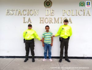 En la fotografía aparece un capturado, junto a personal de Fiscalía General de la Nación y Policía Nacional. En la parte posterior de la imagen se ven banners de Policía Nacional y la Fiscalía General de la Nación.