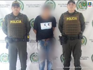 capturdao de frente custodiado por dos policías, Detrás banner de la Policía Nacional.