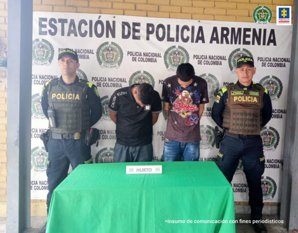 Se observan dos capturados en el centro y a cada costado un funcionario de Policía Nacional. Al fondo un pendón de Policía Nacional y al frente una mesa con el título: hurto
