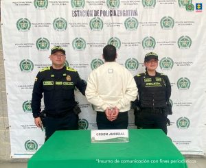 En la fotografía aparece de pie, de espaldas a la cámara, con los brazos atrás y esposado Samuel Castaño García. Viste con buso de mangas largas y color crema, así como pantalón negro. En los extremos hay uniformados de la Policía Nacional. En la parte delantera hay una superficie verde y sobre ella hay un letrero que dice: ‘orden judicial’. En la parte posterior hay un pendón institucional de la Policía.