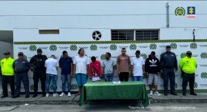 En la fotografía se aprecia de pie a los presuntos integrantes del GDO San Pacho 2. A los extremos del grupo hay uniformados de la Policía Nacional. Delante de ellos hay una mesa con mantel verde y sobre ella hay un letrero con logos de la Policía que dice: ‘Orden judicial’. Detrás de ellos hay un pendón institucional de la Policía.
