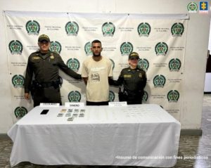 En la fotografía aparece de pie y con los brazos atrás Santiago Andrés Cárdenas Rubio. Viste con camiseta de mangas cortas, de color crema y pantalón oscuro. En sus extremos hay uniformados de la Policía Nacional. Delante de ellos hay una Superficie con mantel blanco y sobre ella se aprecia gran cantidad de bolsas plásticas pequeñas y transparentes, dinero en efectivo y un celular. Detrás de ellos hay un pendón institucional de la Policía.