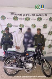 En la fotografía se aprecia de espaldas a la cámara, con los brazos atrás y esposado, Santiago Rosero Ruiz. Viste con buso pantalón de color blanco. A sus extremos hay uniformados de la Policía Nacional. Delante de ellos hay una motocicleta y sobre ella dos letreros que dicen: ‘Captura por hurto’ y ‘Captura en flagrancia’. En la parte posterior hay un pendón institucional de la Policía.