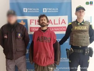 En la fotografía aparece de pie Sebastián Gutiérrez Medina. Presenta barba y bigote poblados. Viste con buso de color rojo, con mangas de color marrón y pantalón oscuro. A su extremo derecho hay un servidor del CTI de la Fiscalía y al derecho un uniformado de la Policía Nacional. Detrás de ellos hay un pendón institucional de la Fiscalía.