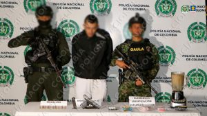 Se observa al capturado de frente, a cada costado un uniformado de Policía Nacional, al frente una mesa con material incautado y atrás un pendón de Policía Nacional.