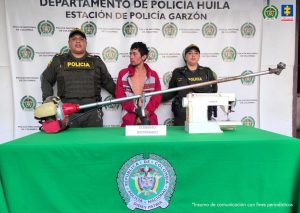El procesado se encuentra esposado y en custodia por uniformados de la Policía Nacional. Detrás suyo un backing de la Policía y se observan los elementos incautados.