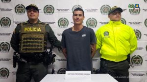 Se visualiza al capturado junto a dos uniformados de la Policía Nacional. Detrás de ellos el banner que identifica a la Policía Nacional.