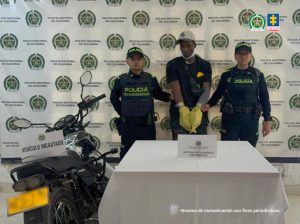  En la foto aparece el capturado de frente y custodiado por dos uniformados de la Policía Nacional. En la foto también aparece un backing de la Policía Nacional y la moto incautada.