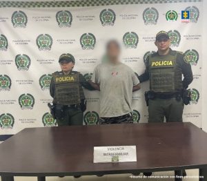 En la fotografía se aprecia de pie y con los brazos atrás a Stiven Alejandro Bríñez Gómez. Viste camiseta de manga corta de color gris; pantalón gris; A sus extremos hay uniformados de la Policía Nacional. Delante de ellos hay una mesa de superficie color marrón y sobre ella un letrero que dice: ‘Violecia intrafamiliar’. Detrás de ellos hay un pendón institucional de la Policía.