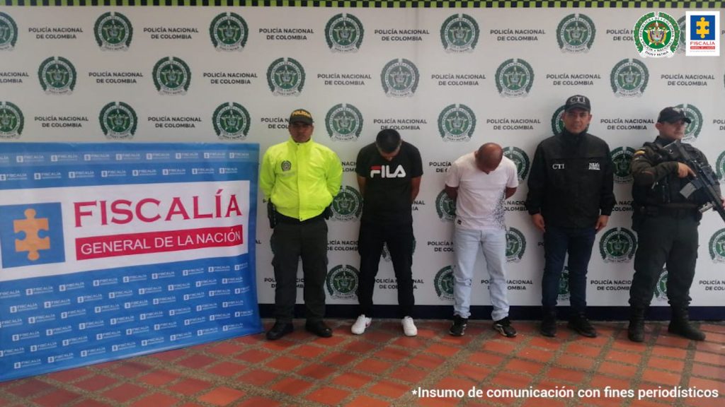 Se observa a dos capturados de frente. A un lado un funcionario del CTI y en el otro uno de Policía Nacional. Al fondo backing de Policía Nacional