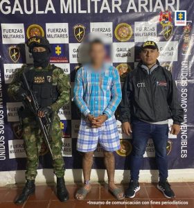 En la foto esta el capturado esposado mirando de frente, con camisa , pantaloneta y chancletas, custodiado por un militar del Gaula del Ejército Nacional y un investigador del CTI de la Fiscalía.Detrás de ellos un banner de fiscalía y ejército Nacional.