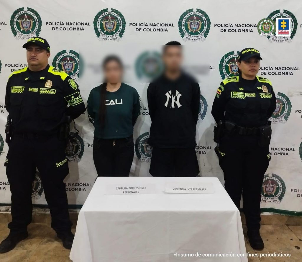 Se observan los dos capturados e frente y con un efecto que difumina sus rostros. A cada costado un funcionario de Policía Nacional. Atrás un pendón de Policía Nacional