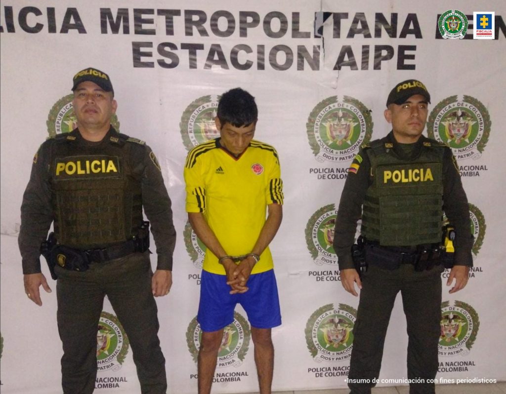 En la fotografía aparece un capturado, junto a personal de Policía Nacional. En la parte posterior de la imagen se ven banners de Policía Nacional y la Fiscalía General de la Nación.