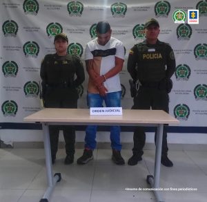 En la fotografía se aprecia a Víctor Raúl Monsale Moreno, alias Chocherita, de pie, con los brazos adelante y esposado. Viste camiseta blanca de manga corta con una franja gruesa negra a la altura del pecho y una franja ancha vertical color café; así como jean azul y zapatos oscuros. A lado y lado de él hay uniformados de la Policía Nacional. Delante de ellos hay una mesa y sobre ella un letrero que dice: ‘Orden judicial’. Detrás de ellos hay un pendón institucional de la Policía. 