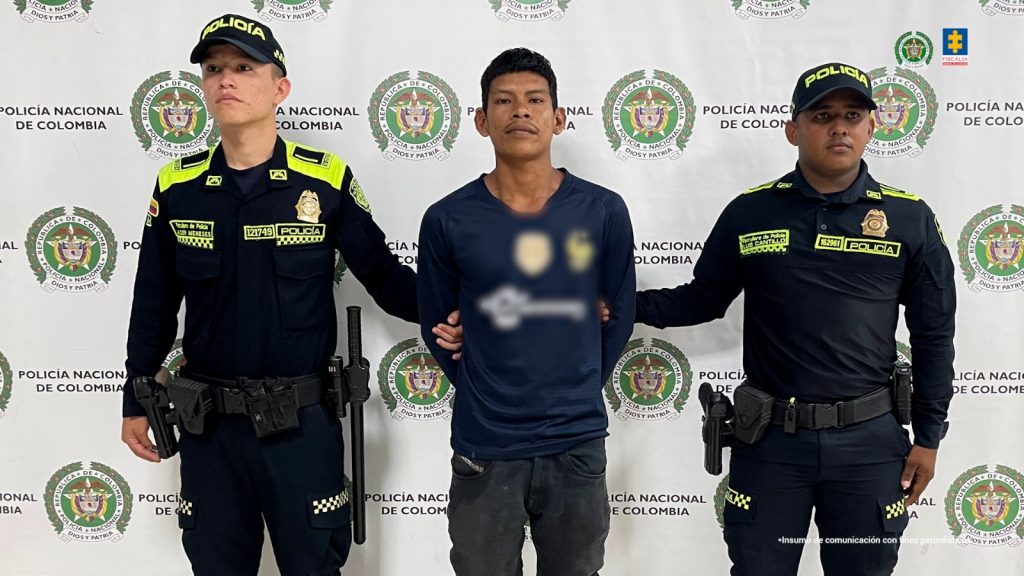 En la foto se observa al capturado custodiado por dos uniformados de la Policía Nacional. Detrás hay un backing de la Policía Nacional.