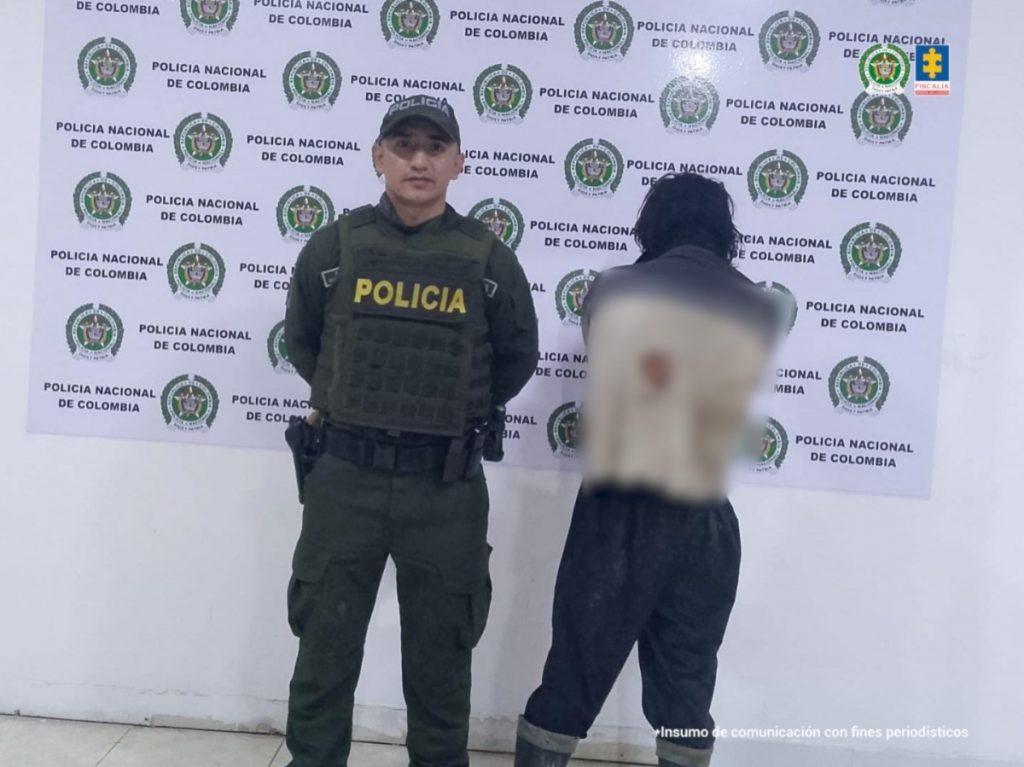 En la foto aparece el capturado de espalda y custodiados por un uniformado de la Policía y Ejército Nacional. De fondo aparece un backing de la Policía Nacional.