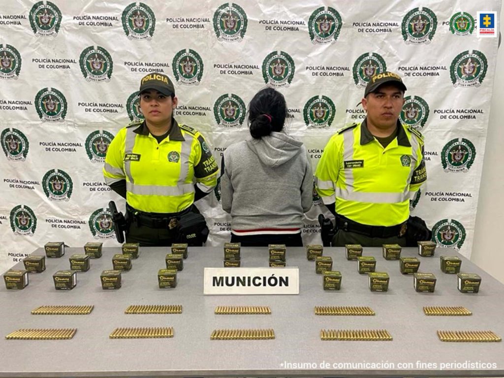 En la foto aparece, de espalda, Wendy Tatiana Ortega, vestida con un buzo gris con capucha. A lado y lado de ella hay dos uniformados de la Policía Nacional. Delante de ellos hay una mesa gris y sobre ella munición y cajas pequeñas; asimismo, un letrero que dice ‘munición’. Detrás de ellos hay un pendón institucional de la Policía.
