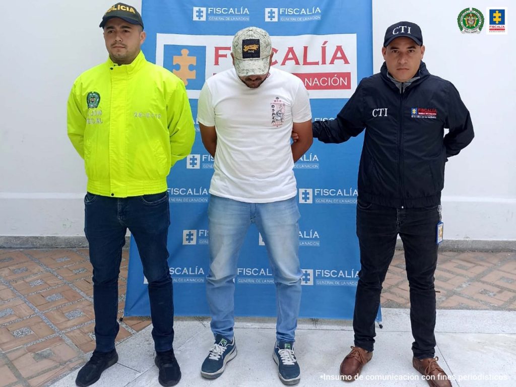 En la fotografía Carlos Arturo Cuesta, alias Alicate, al lado de dos uniformados del CTI y la Policía Nacional. Atrás el banner con logos de la Fiscalía General de la Nación.