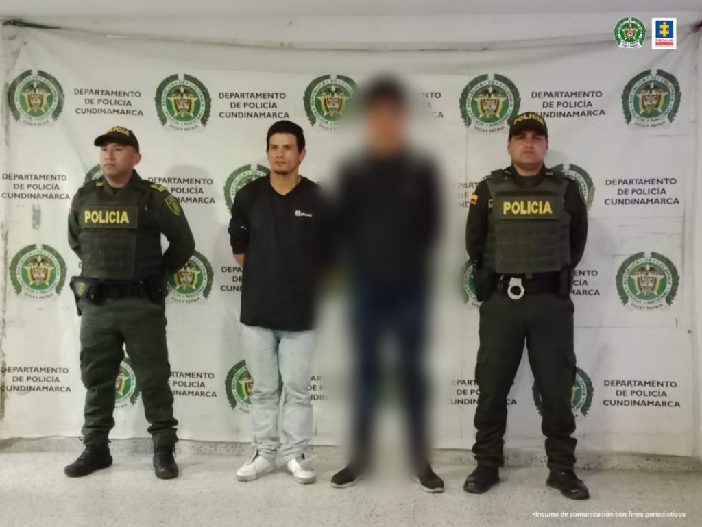Hombre capturado que viste camiseta negra y Jeans azul claro, en posición de pie, con las manos atrás y en el medio de dos funcionarios de la Policía Nacional.