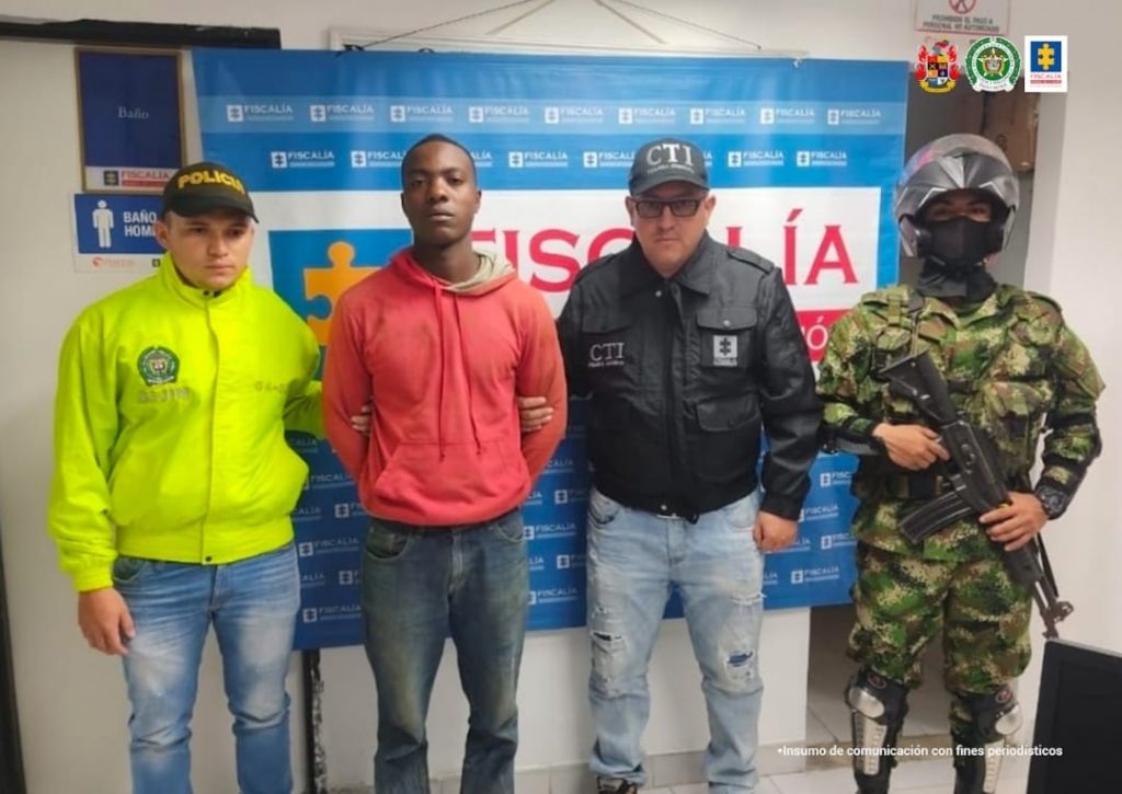 En la fotografía se observa al capturado junto a un servidor del CTI, un agente de la Policía y un soldado del Ejército Nacional. En la parte superior se observa un banner de la Fiscalía General.