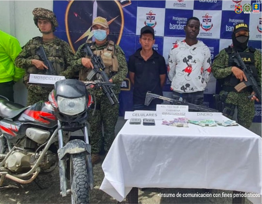 En la fotografía se observan a los dos capturados junto a dos unidades de la Armada Nacional, un integrante del Gaula Militar y dos agentes de la Policía Nacional. En la parte posterior se observa una mesa con un fusil, teléfonos celulares y dinero en efectivo.