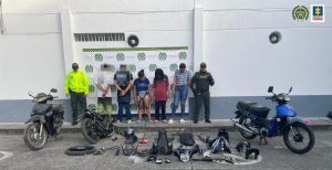 En la foto aparecen en hilera, de frente y con la cabeza agachada las tres mujeres imputadas. A lado y lado de ellas hay uniformados de la Policía Nacional. Delante de ellos hay tres motocicletas completas y en el piso partes de otra. Detrás de ellos hay un pendón institucional de la Policía.