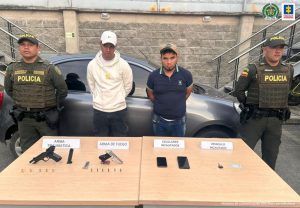Se observan dos capturados al centro y en los extremos funcionarios de Policía nacional. detrás un vehículo y adelante una mesa con el material incautado