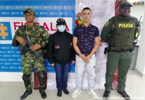 En la fotografía se observa al capturado junto a un servidor del CTI, un agente de la Policía Nacional y un soldado del Ejército Nacional. En la parte superior se observan un banner de la Fiscalía General y otro banner del Ejército Nacional