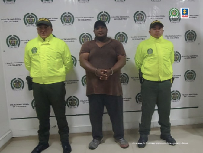 en la foto el hmbre de camisa oscura con esposas acompañado de dos uniformados de la policóa Nacional