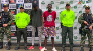 En la foto aparecen Malcon Seanckler Salamanca Cabrera y Yivinson Alexander Cuesta Mena acompañados por un funcionario del CTI de la Seccional Chocó y atrás el backing con logos de la Fiscalía.