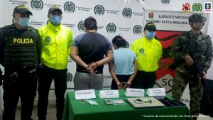 En la imagen se observa a dos personas custordiadas por policía Nacional y ejército, frente a ellos una mesa con elementos incautados.