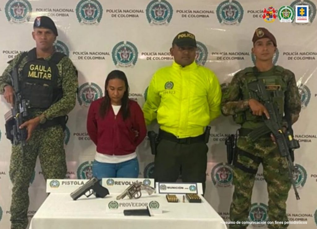 En la fotografía se observa a la capturada junto a un agente de la Policía a y a dos soldados del Gaula Militar. En la parte posterior se observa una mesa con dos armas de fuego, un proveedor y munición.