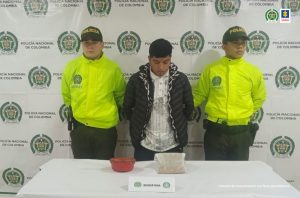 Fiscalía judicializó a una pareja que transportaba marihuana en un vehículo y a un hombre capturado con morfina En la fotografía se al capturado junto a dos agentes de la Policía Nacional. En la parte posterior se observan una mesa con una olla de plástico y una bolsa con morfina