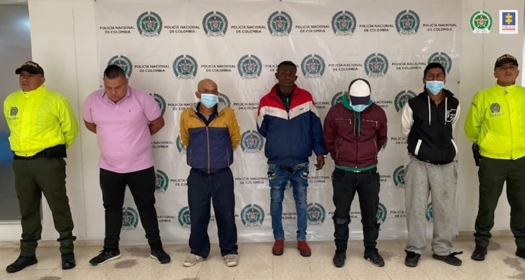 En la fotografía se observa los cinco capturados junto a dos agentes de la Policía Nacional. En la parte superior se observa un banner de la Policía