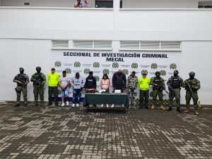 En la foto aparecen, de pie los presuntos integrantes del grupo delictivo ‘Clan del Golfo’. A lado y lado de ellos hay uniformados de la Policía y de la Armada Nacional. Delante de ellos hay una mesa con mantel verde y sobre ella varios elementos incautados. Detrás de ellos hay un pendón institucional de la Policía.