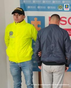 En la fotografía se observa la captura junto a un servidor del CTI y a un agente de la Policía Nacional. En la parte superior se observa un banner de la Fiscalía General de la Nación