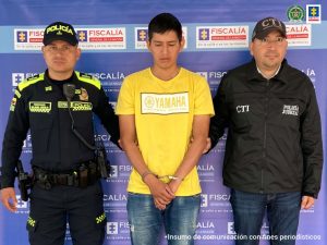 En la fotografía se observa al capturado junto a un servidor del CTI y un agente de la Policía Nacional. En la parte superior se observa un banner de la Policía Nacional