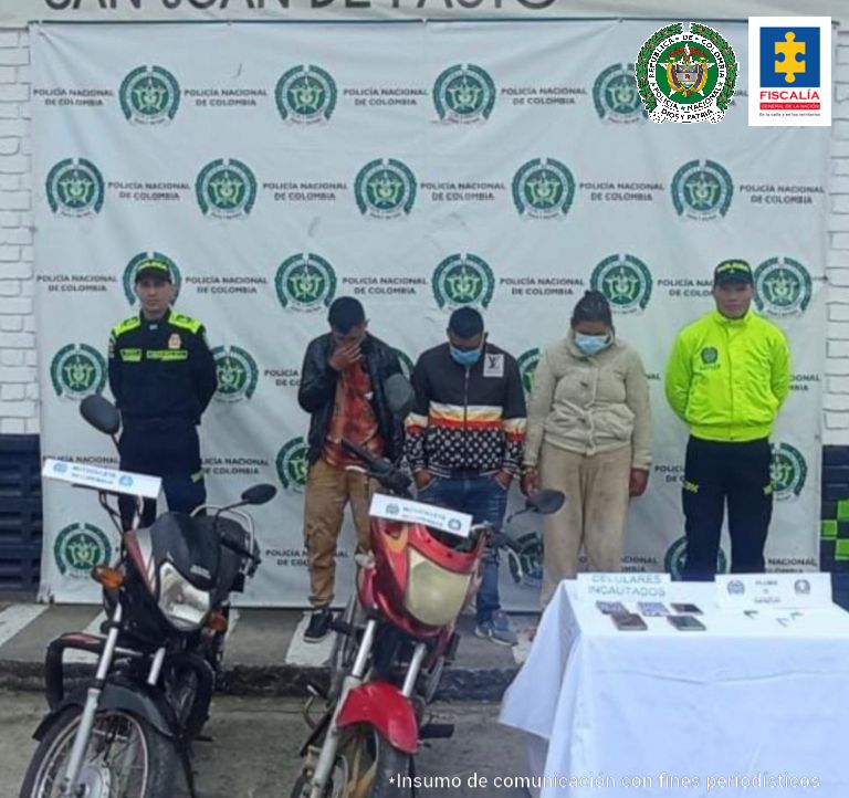 En la fotografía se observa a los tres capturados junto a dos agentes de la Policía Nacional. En la parte posterior se observa una mesa con 5 teléfonos celulares, dosis de cocaína rosada y dos motocicletas. 