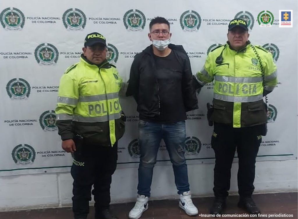 En la fotografía se observa al capturado junto a dos agentes de la Policía Nacional. En la parte posterior se observa un banner de la Policía Nacional