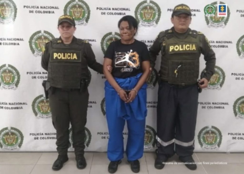 En la fotografía se observa a la capturada junto a dos agentes de la Policía. En la parte superior se observa un banner de la Policía Nacional