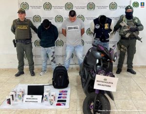 En la fotografía se observan los tres capturados junto a dos agentes de la Policía Nacional. En la parte posterior se observa un maletín, un computador portátil, 5 teléfonos celulares, 9 cajas de empacar móviles y una motocicleta