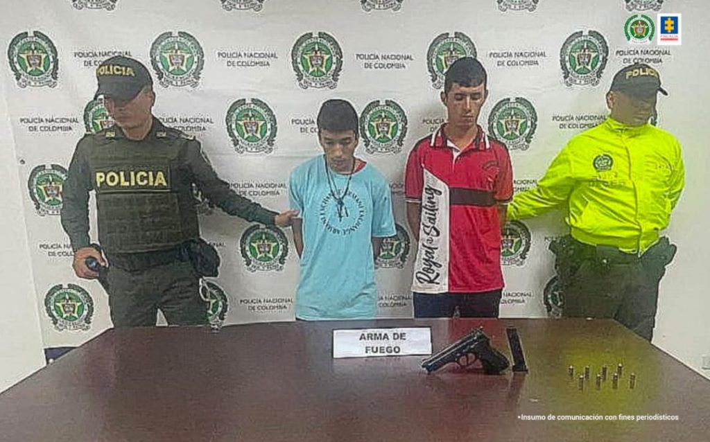 En la foto aparecen, con los brazos atrás, Mauricio Lindo Bedoya y Jhon Nerly Salazar Torres. Uno de ellos viste camiseta azul claro con dibujo circular a la altura del pecho; collar negro. El otro viste camisa de manga corta roja con franja vertical blanca gruesa al lado derecho e él y franja negra a la altura del pecho, al lado izquierdo; asimismo, pantalón negro. A lado y lado de ellos hay uniformados de la Policía Nacional. Delante de ellos hay una mesa y sobre ella hay un arma de fuego, un proveedor y munición; también hay un letrero que dice: Arma de fuego. Detrás de ellos se ve un pendón institucional de la Policía.