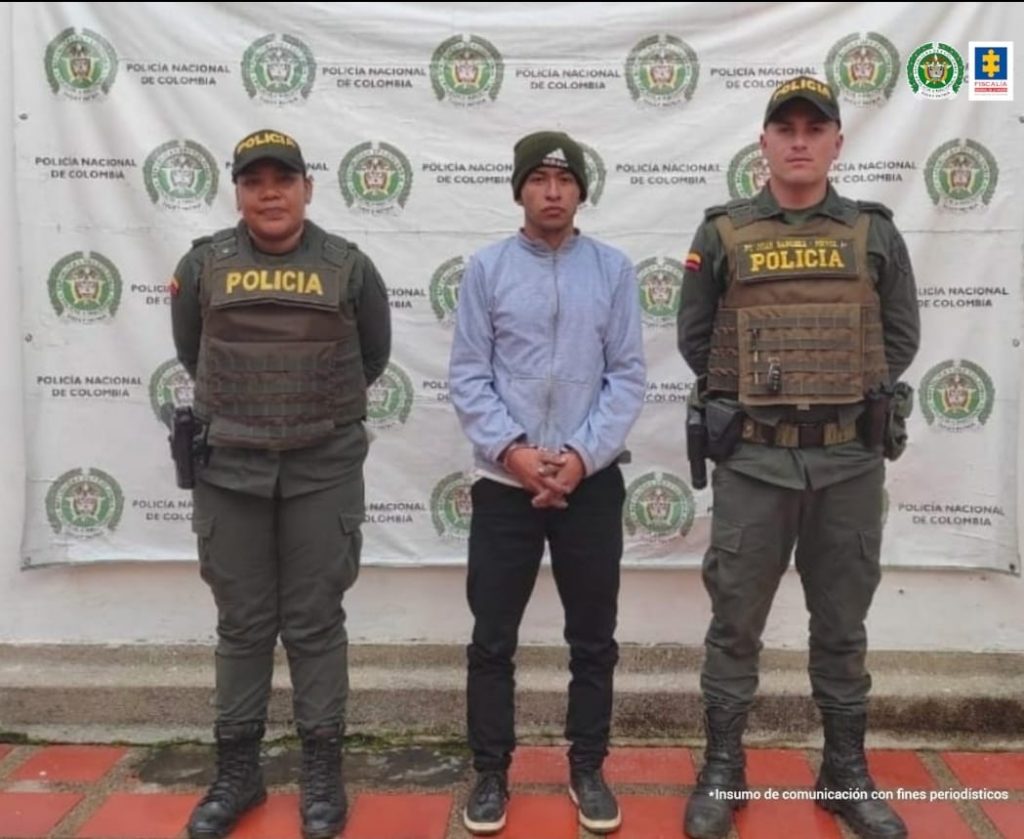 En la fotografía se observa al capturado junto a dos agentes de la Policía Nacional. En la parte superior se observa un banner de la Policía Nacional