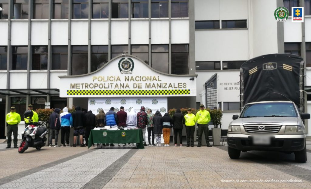 En la foto se ve al fondo a los detenidos, y sobre la mesa de mantel verde con escudos de la Policía Nacional estupefacientes, dinero, celulares y un arma de fuego.