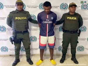 En la fotografía se observa al capturado junto a dos agentes de la Policía Nacional. En la parte superior se observa un banner de la Policía Nacional