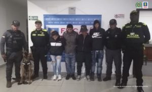 En la fotografía se observan los cuatro capturados junto a dos agentes de la Policía Nacional. En la parte superior se observa un banner de la Fiscalía General de la Nación
