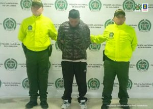 En la fotografía se observa al capturado junto a dos agentes de la Policía Nacional. En la parte superior se observa un banner de la Policías Nacional